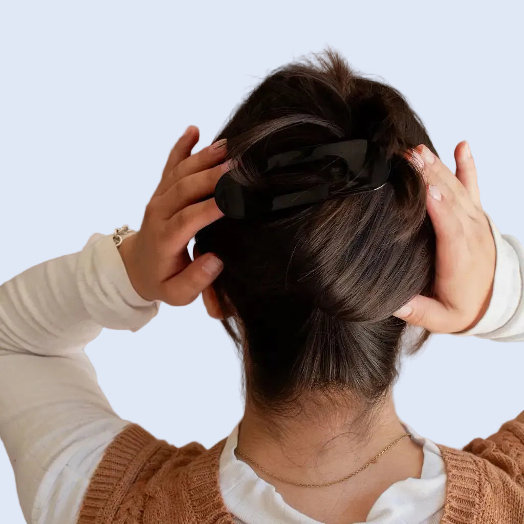 Person adjusting a black hair tie in their hair against a neutral background