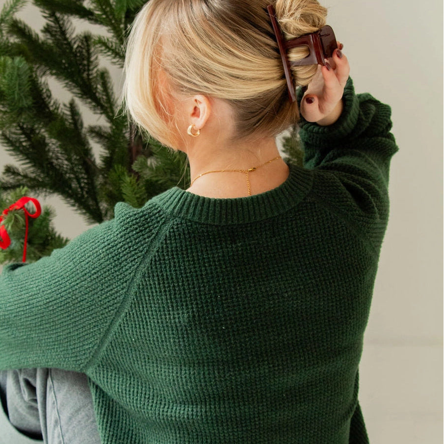 Person wearing a green sweater sitting in front of a decorated Christmas tree.