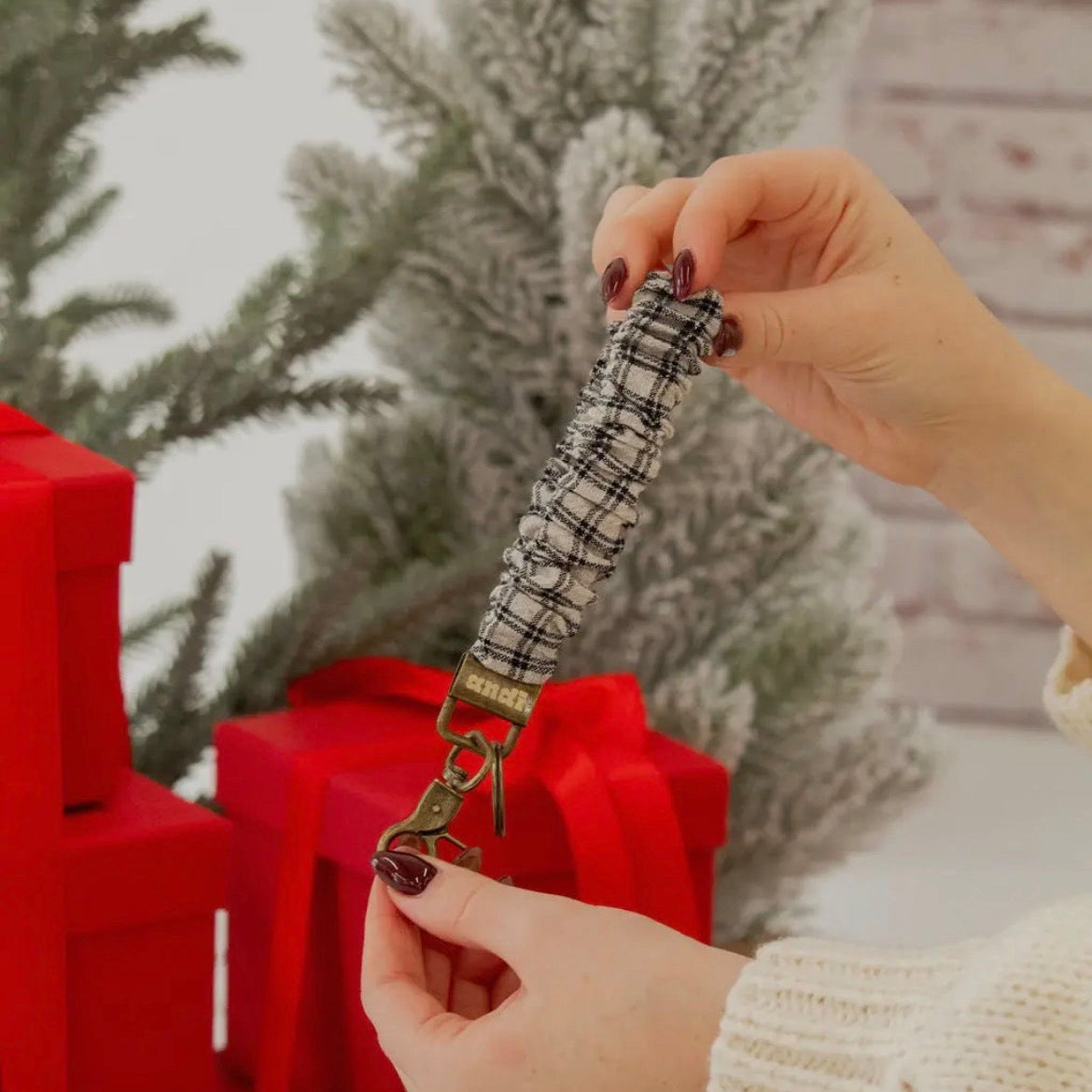 Hand holding a plaid lanyard with a Christmas tree and presents in the background