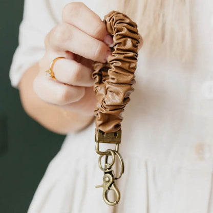 I'm holding a brown scrunchie keychain with a gold clasp against a neutral background