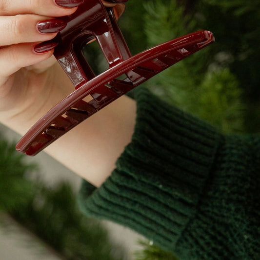Hand holding a red hair clip with a blurred green background
