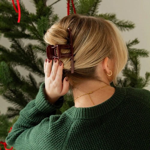 Person adjusting a hair clip in front of a Christmas tree
