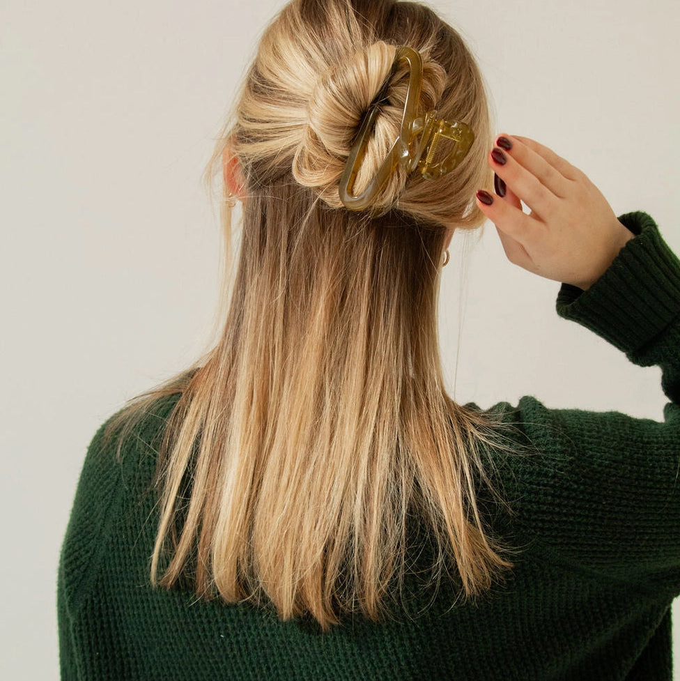 Person adjusting a gold hair accessory in their blonde hair against a plain background