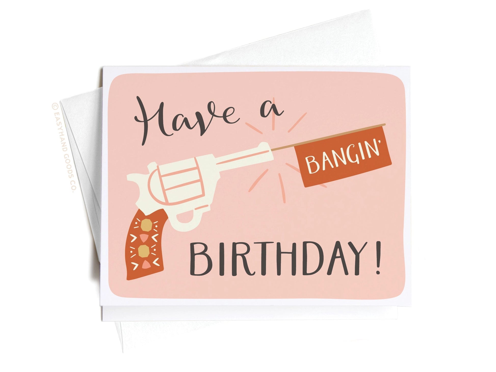 Hand holding a birthday card with a gun graphic and text on a pink background saying have a bangin birthday