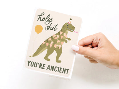Notebook with a dinosaur illustration and humorous text held by a hand on a white background