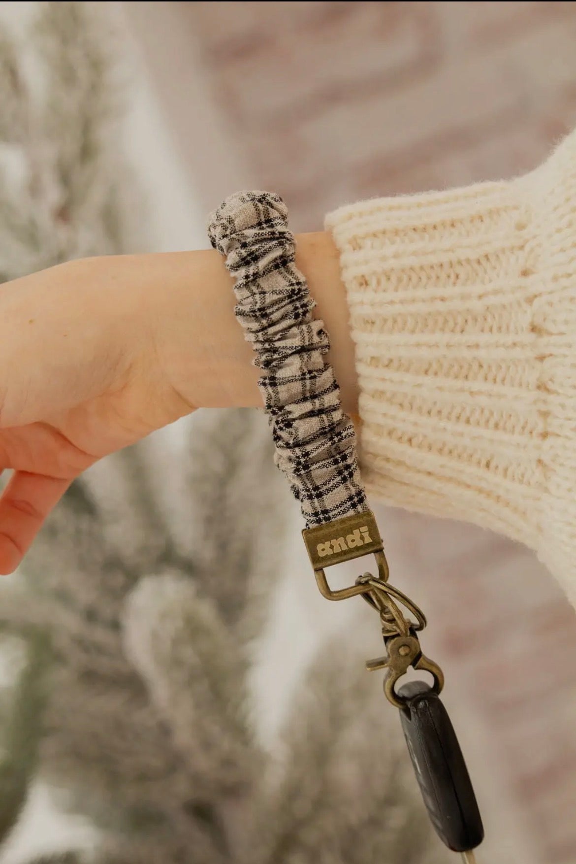 Plaid lanyard with Coach logo held by a person wearing a beige sweater.