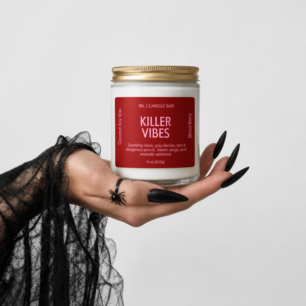 A hand with long black nails and a black lace sleeve holds a candle jar labeled 'Killer Vibes' by Helly Candle Bar against a light gray background.