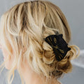 Black hair clip with gold accents in blonde hair against a neutral background