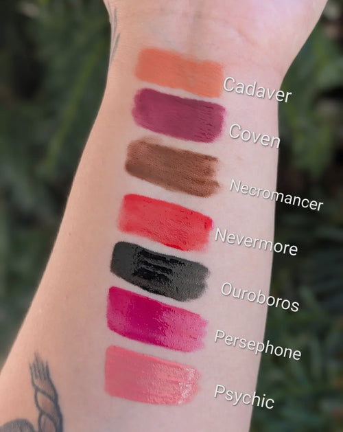 Lipstick swatches on a person's arm with labeled colors against a blurred natural background