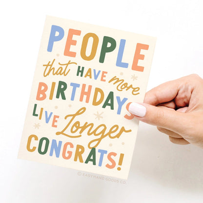 Hand holding a colorful birthday card with humorous text on a white background