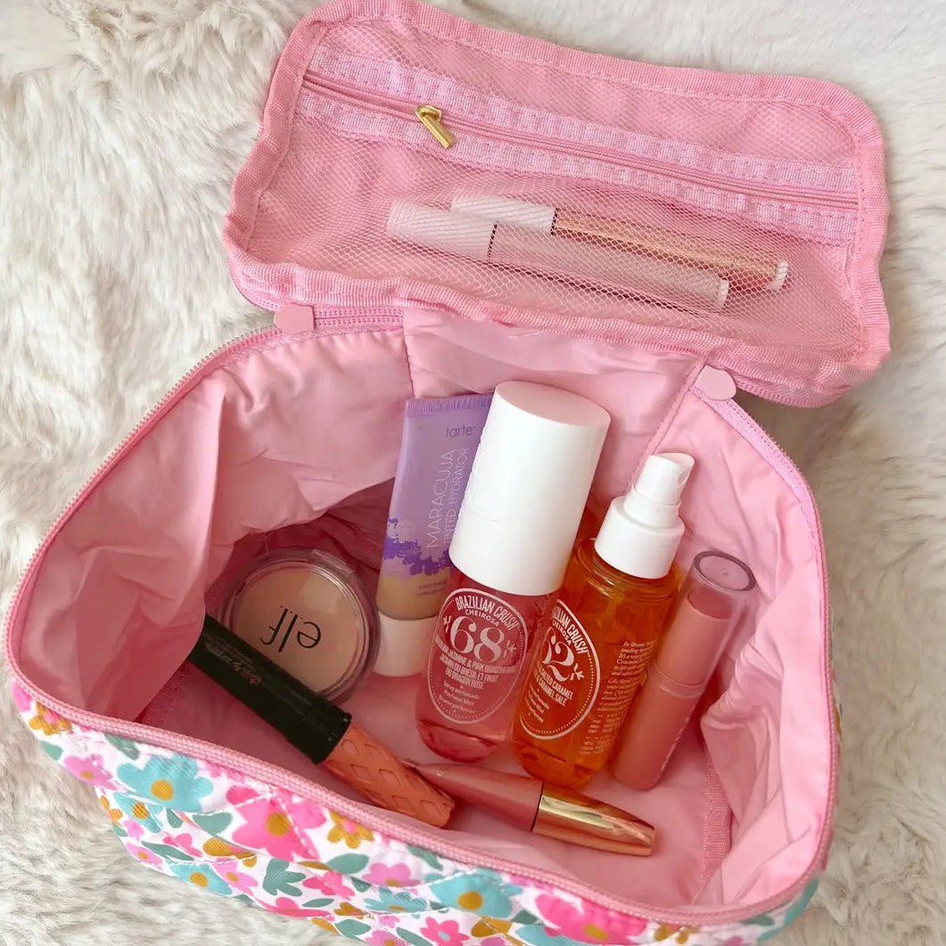 Pink floral makeup bag with various cosmetic products on a white fur surface