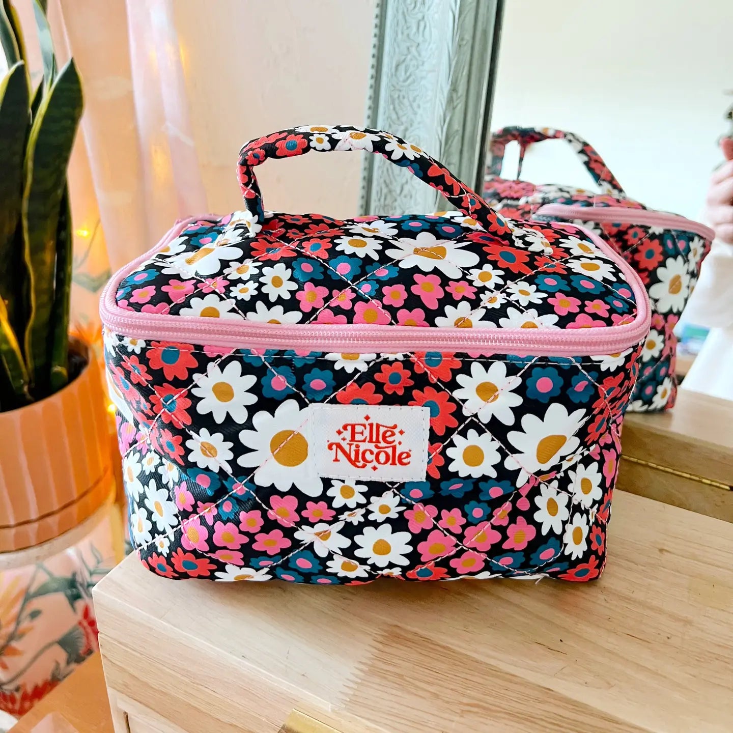 Floral patterned cosmetic bag with pink accents on a wooden surface