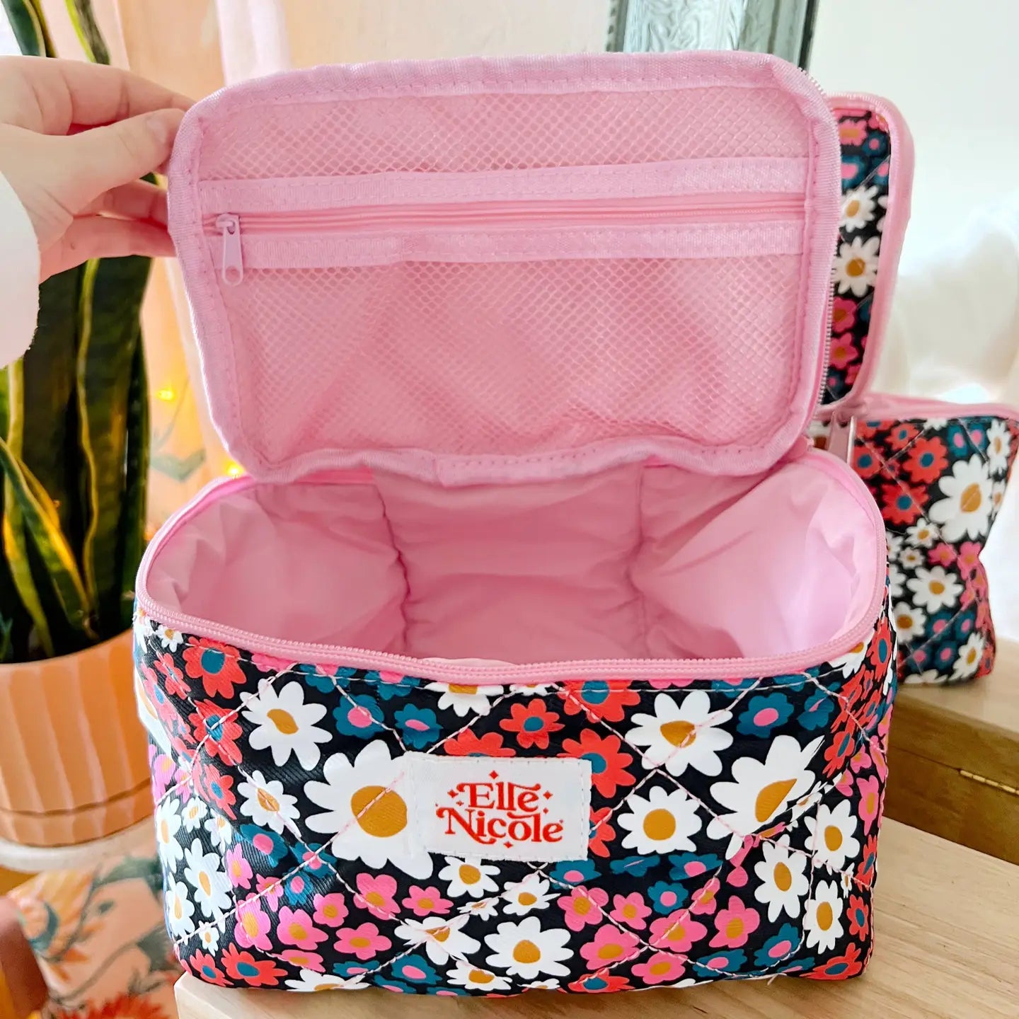 Floral-patterned makeup bag with pink interior, held open by a hand.