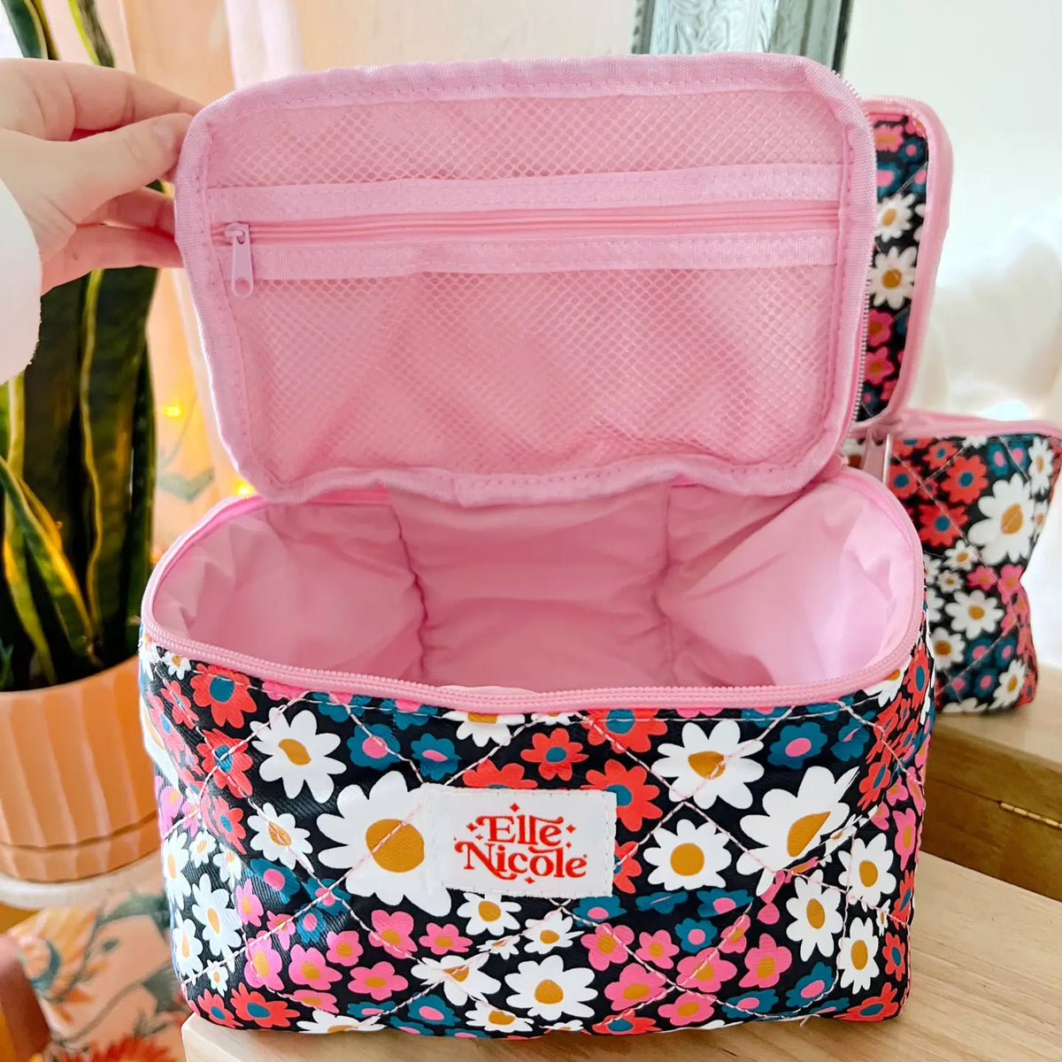 Floral-patterned makeup bag with pink interior, held open by a hand.
