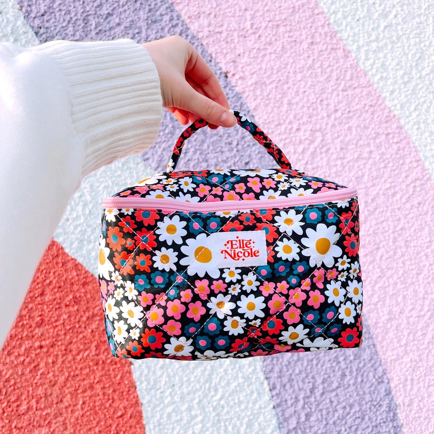 Floral patterned bag with 'Elle & Nicole' branding held by a person against a colorful background.