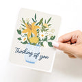 Card with floral design and 'Thinking of you' text held by a hand on a white background