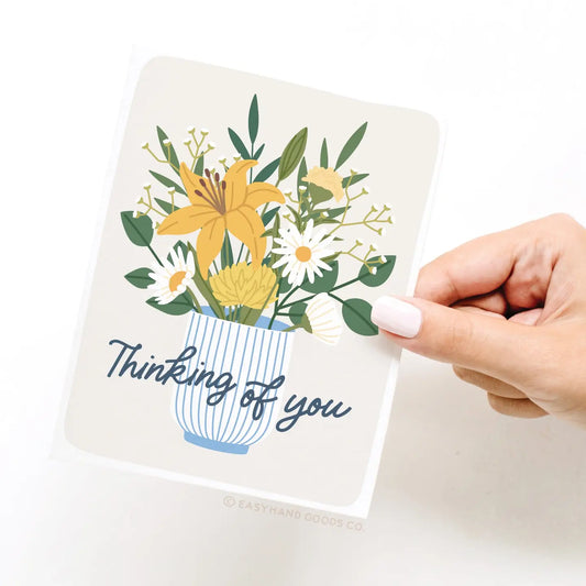 Card with floral design and 'Thinking of you' text held by a hand on a white background