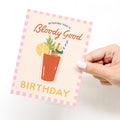Hand holding a birthday card with a Bloody Mary illustration and text on a white background